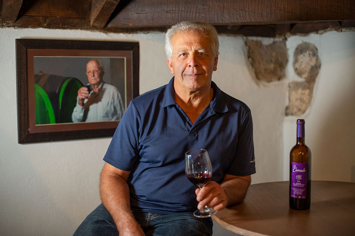 Uomo che tiene un bicchiere di vino accanto a bottiglia e ritratto nella cantina di Tenerife.