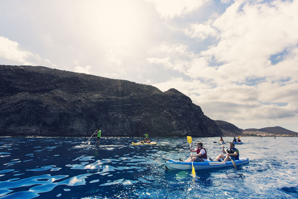 Persone che fanno kayak e paddle surf sulla costa di Tenerife con montagne sullo sfondo.