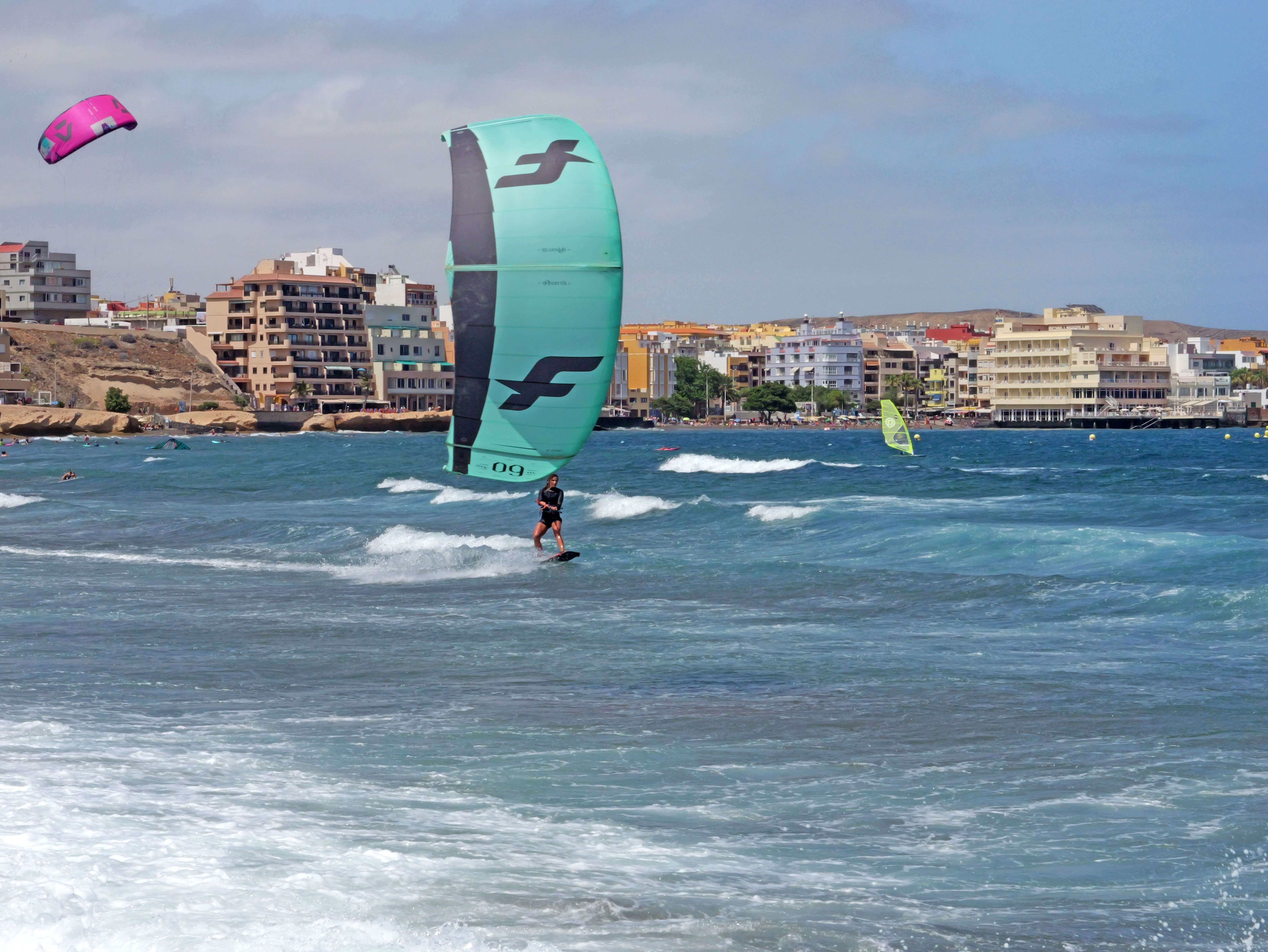 Persona che fa kitesurf sulla spiaggia con gli edifici di El Médano sullo sfondo.