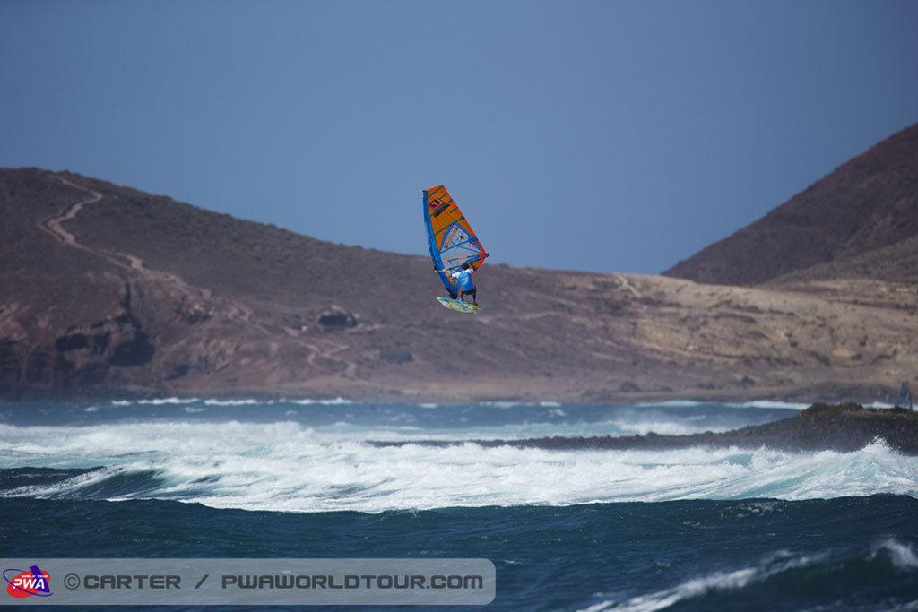 Windsurfista in volo a El Médano, Tenerife, con onde e montagne sullo sfondo.