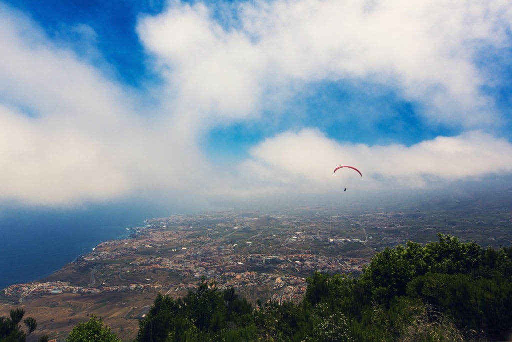 Parapendio che sorvola il paesaggio costiero di Tenerife sotto un cielo parzialmente nuvoloso.
