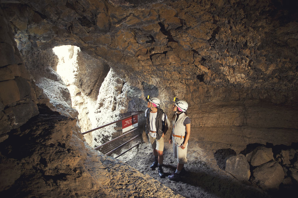 Due persone con elmetti esplorano una grotta a Tenerife, con la luce naturale che filtra.