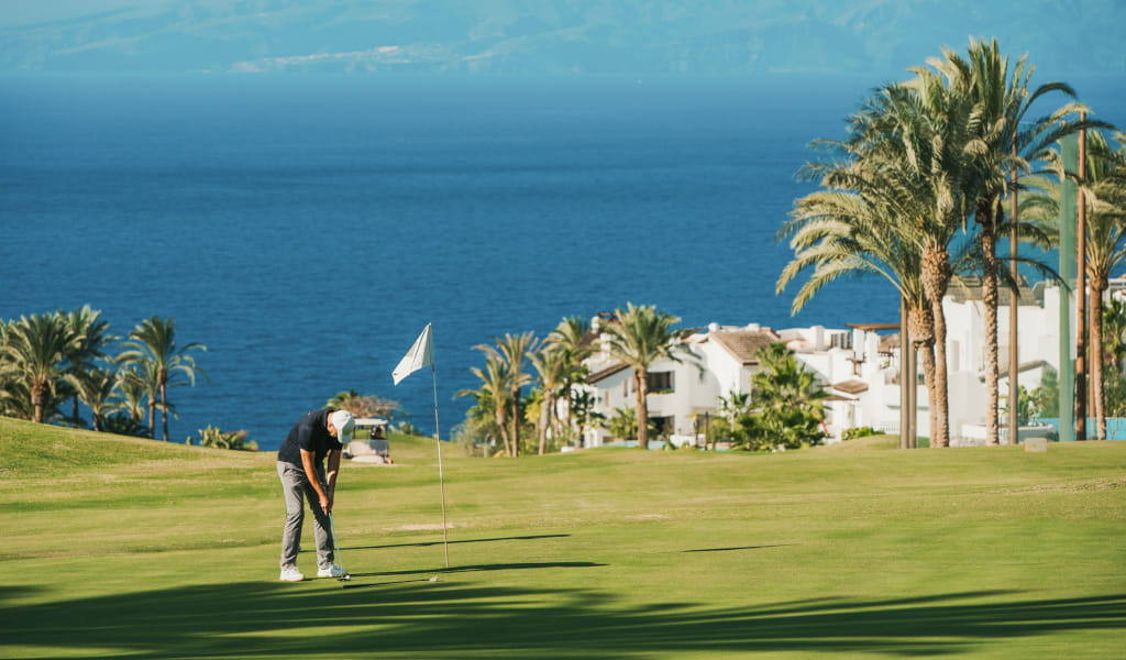 Persona che gioca a golf su un campo con vista sul mare e case a Tenerife.