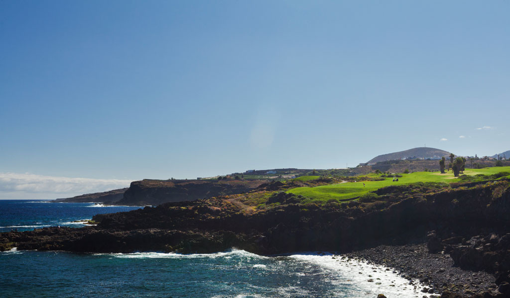 Costa rocciosa e campagna verde a Tenerife che si affaccia sul mare sotto un cielo limpido.