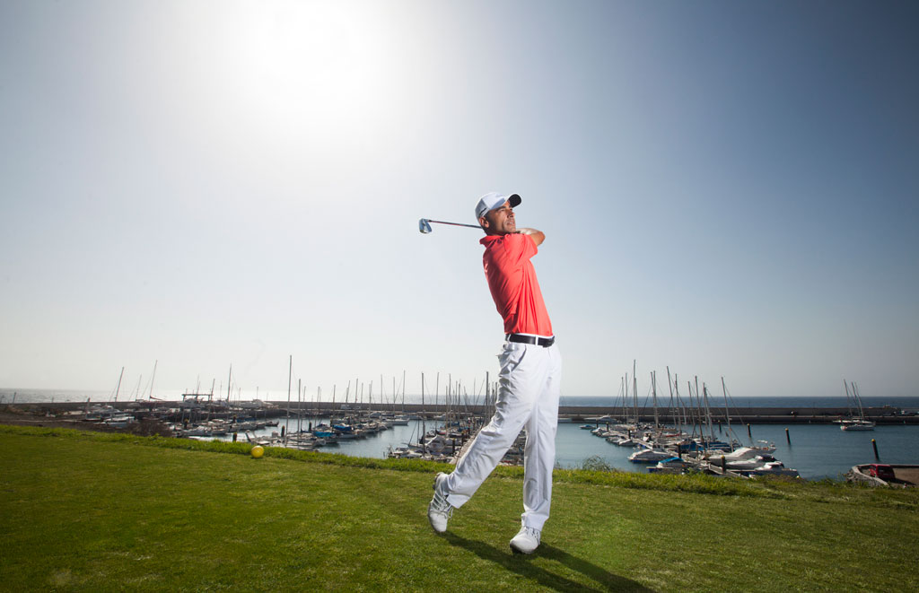 Golfista durante uno swing con marina e barche sullo sfondo a Tenerife.