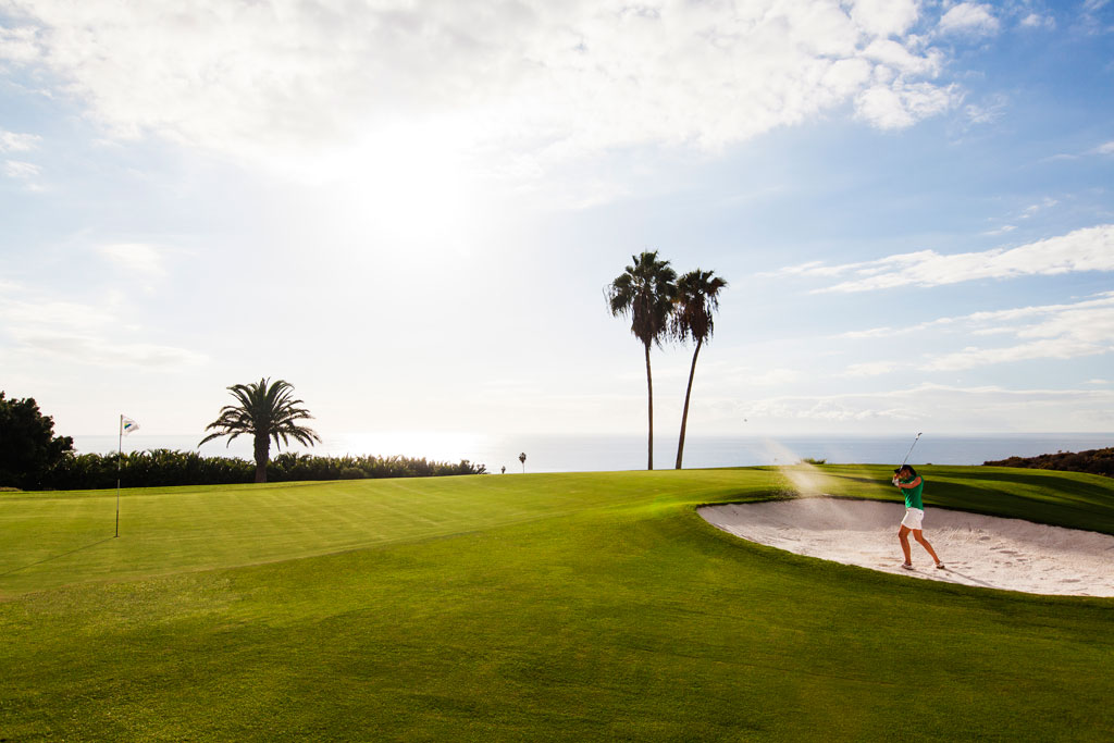 Persona che gioca a golf su un campo sul mare a Tenerife con palme e cieli limpidi.