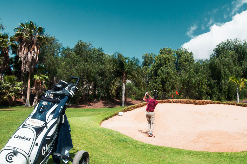 Golfista in azione su un campo a Tenerife, vicino a un bunker.