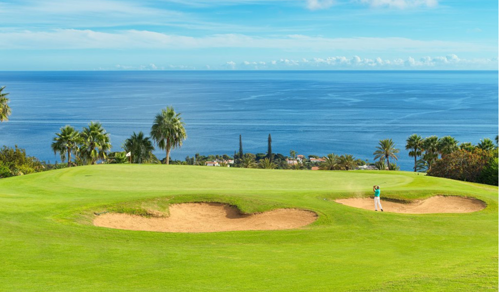Campo da golf a Tenerife con vista sull'oceano. Colpi vicino a bunker circondati da palme.