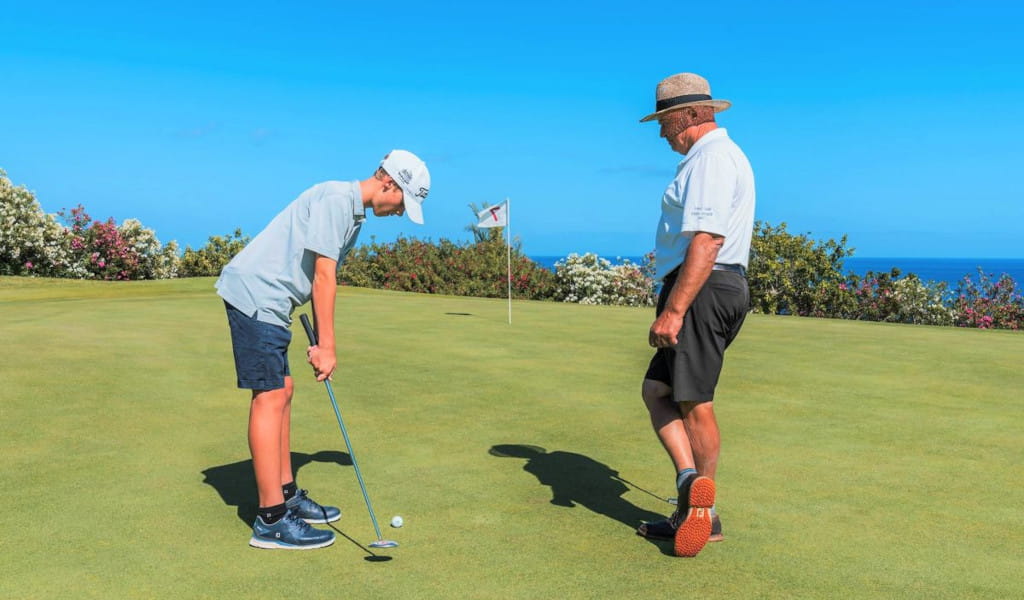 Bambino che gioca a golf con un adulto sullo sfondo, Tenerife.