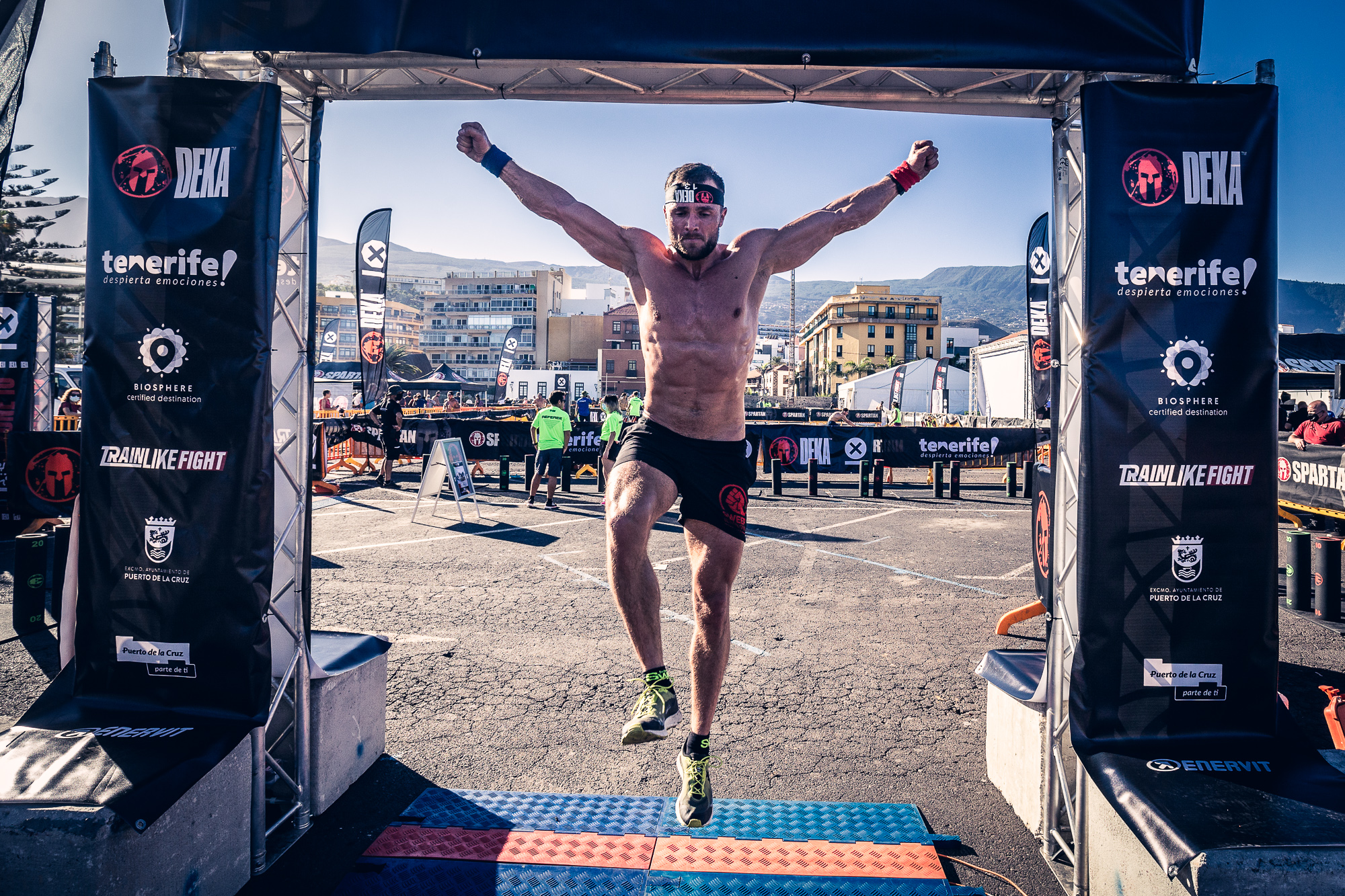 Atleta che taglia il traguardo nella competizione di Tenerife, con striscioni e sfondo urbano.