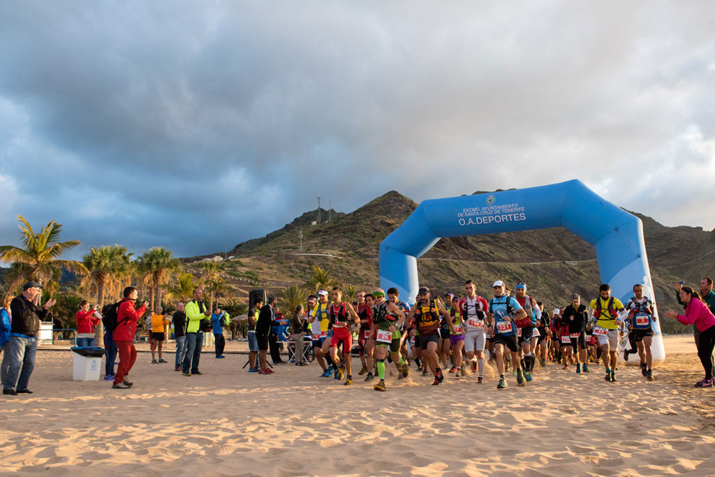 Corridori che iniziano una maratona sulla spiaggia di Las Teresitas, Tenerife, sotto un arco blu.
