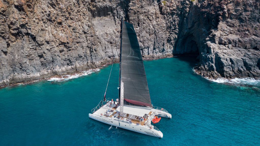 Catamarano che naviga vicino a scogliere rocciose sulla costa di Tenerife.