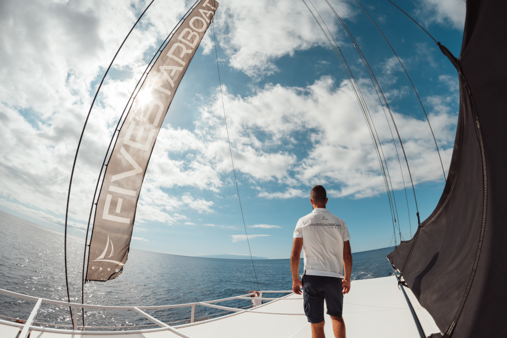 Persona sulla prua di una barca con una maglietta con scritto FIVESTARBOAT, che guarda il mare a Tenerife.