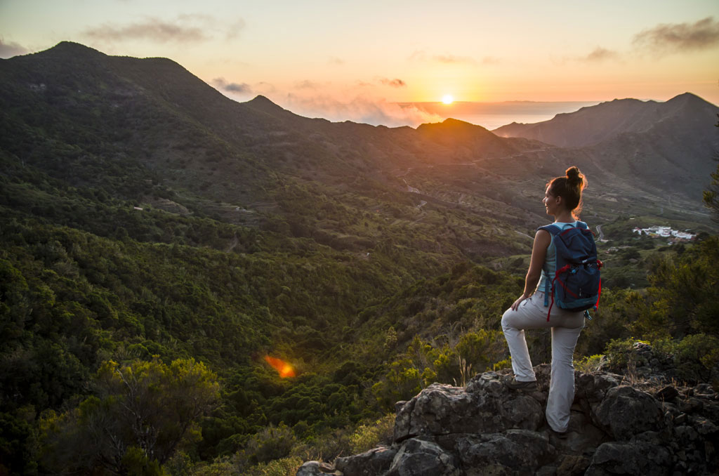 Una persona con lo zaino osserva il tramonto da un punto di vista sulle montagne di Tenerife.