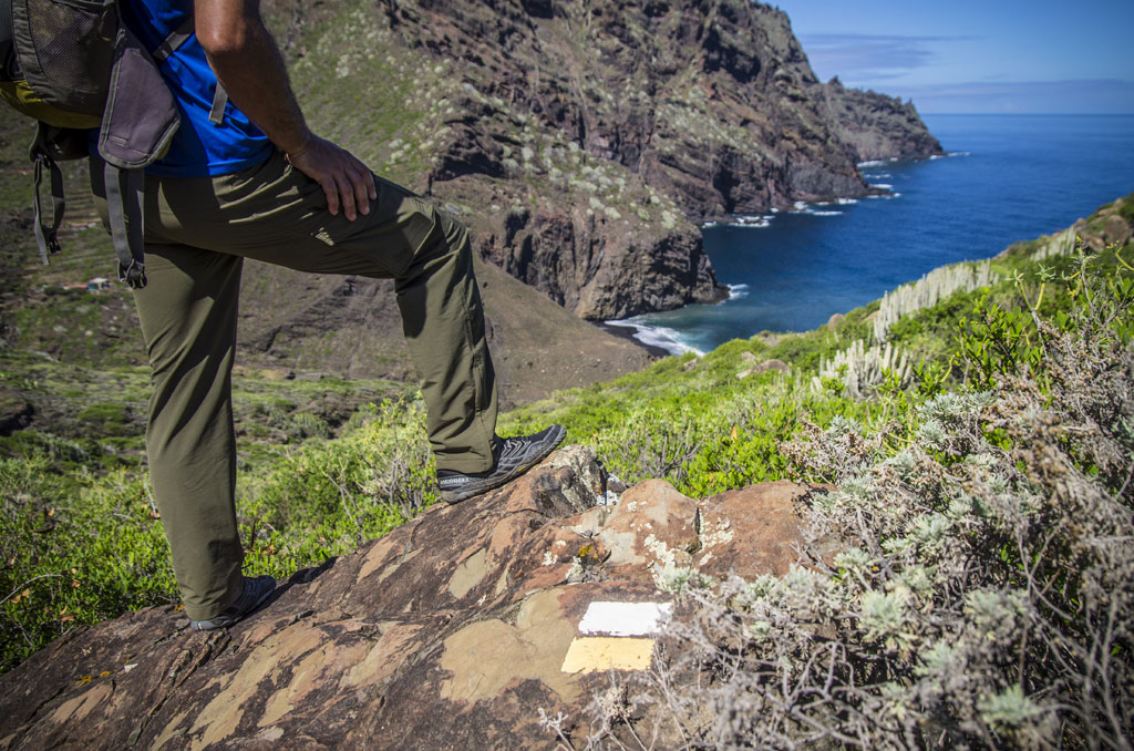 Persona con zaino su una roccia su un sentiero a Tenerife con vista sul mare.
