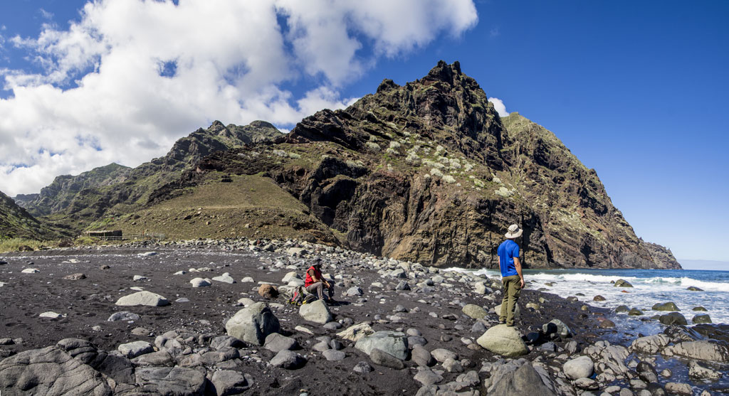 Persone sulla spiaggia di sabbia nera con montagne sulla costa di Tenerife.