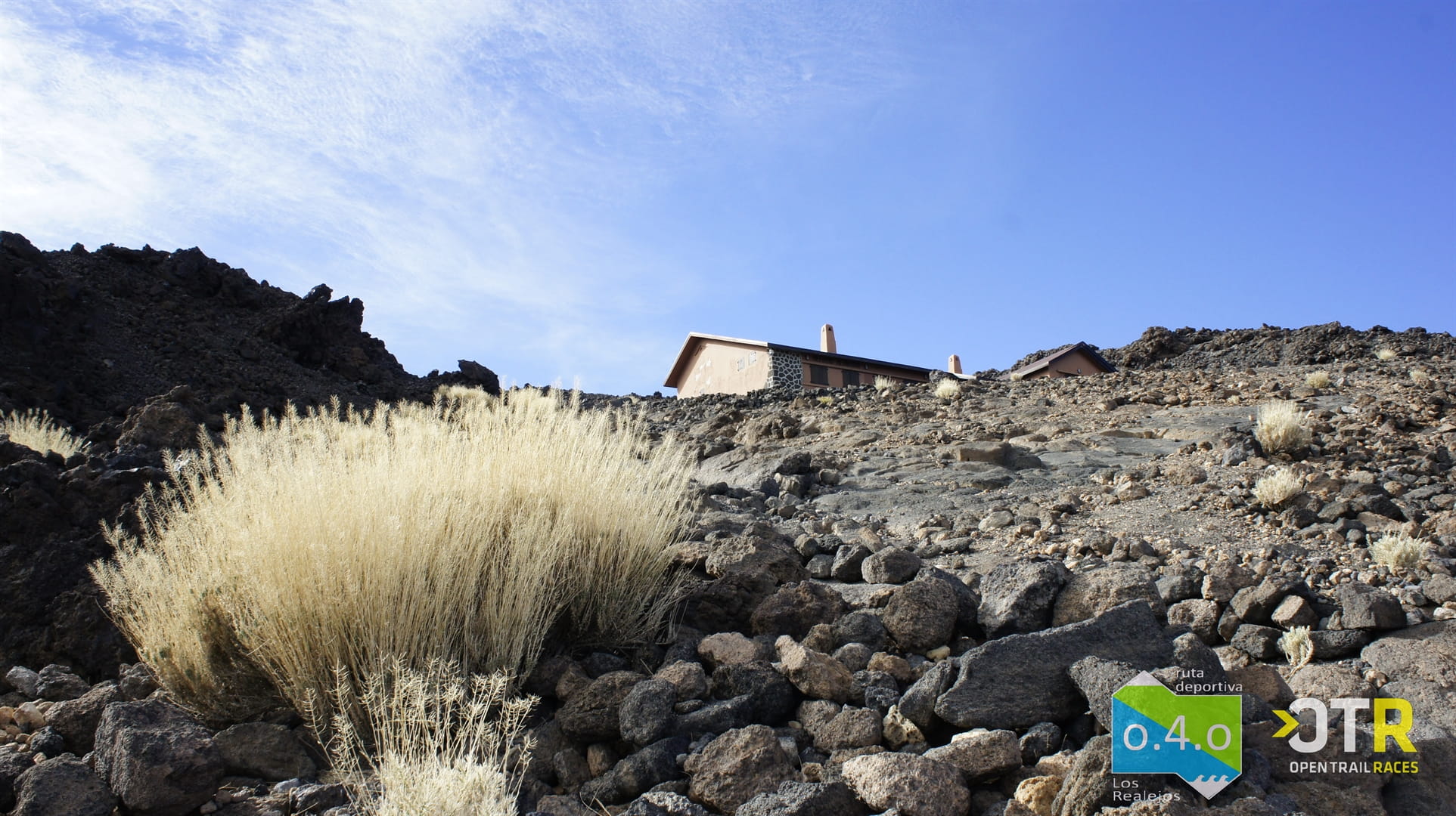 Paesaggio roccioso con edifici su El Teide, Tenerife, cielo limpido, logo OTR visibile.