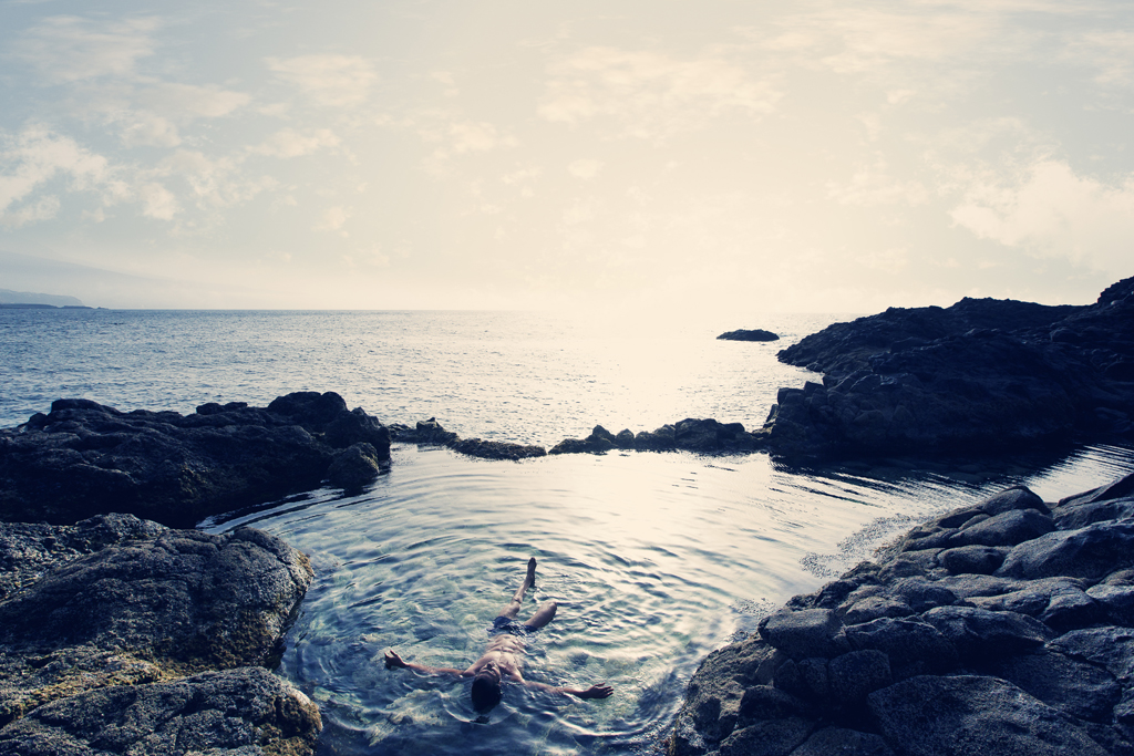 Persona che galleggia in una piscina naturale circondata da rocce vicino all'oceano a Tenerife.