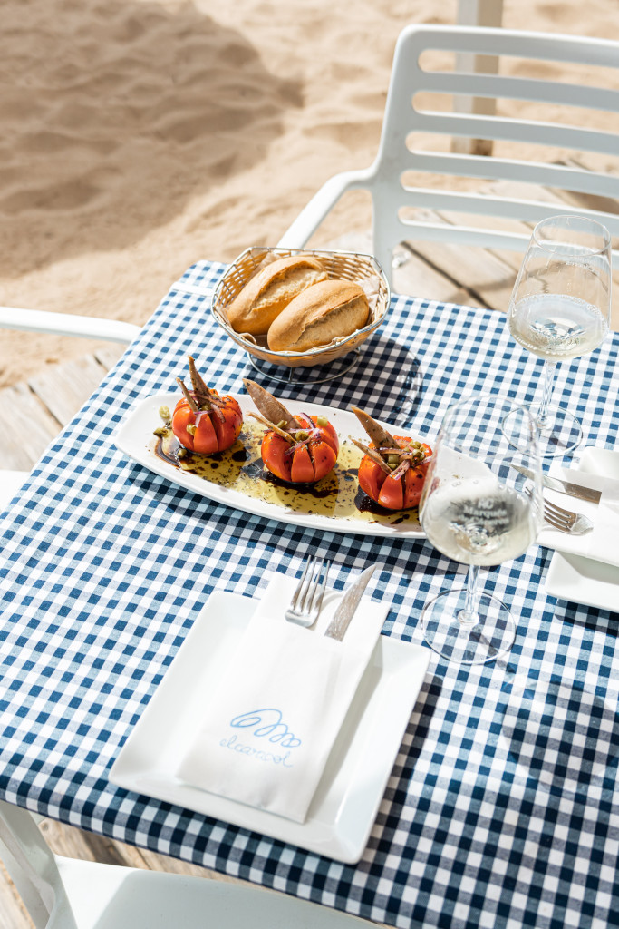 Tavolo con pomodori ripieni, pane e bicchiere di vino davanti alla spiaggia di El Ancla a Tenerife.
