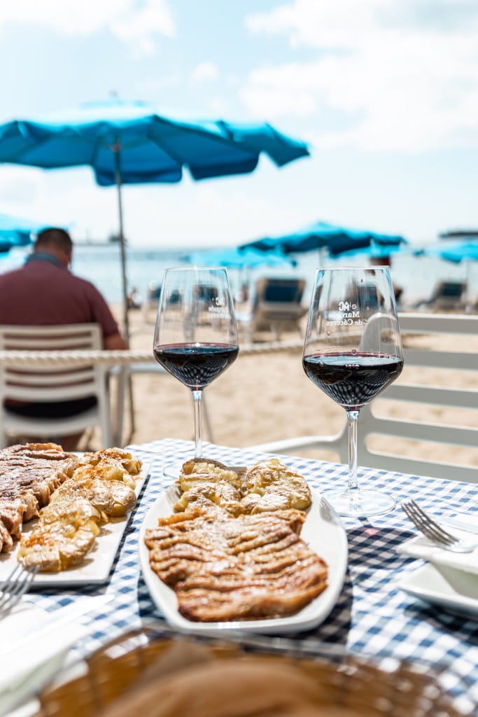 Bicchieri di vino e cibo sulla spiaggia con ombrelloni blu a Tenerife.