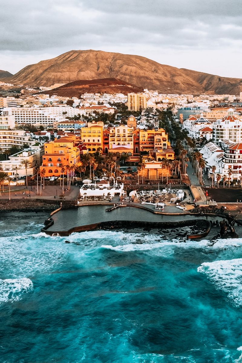 Veduta aerea della costa di Tenerife con edifici e montagna sullo sfondo.