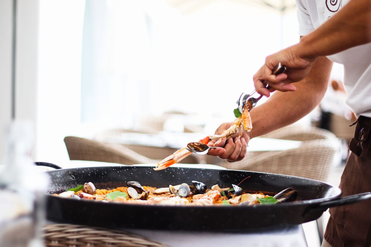 Persona che serve pesce in una paella su terrazza di un ristorante a Tenerife.