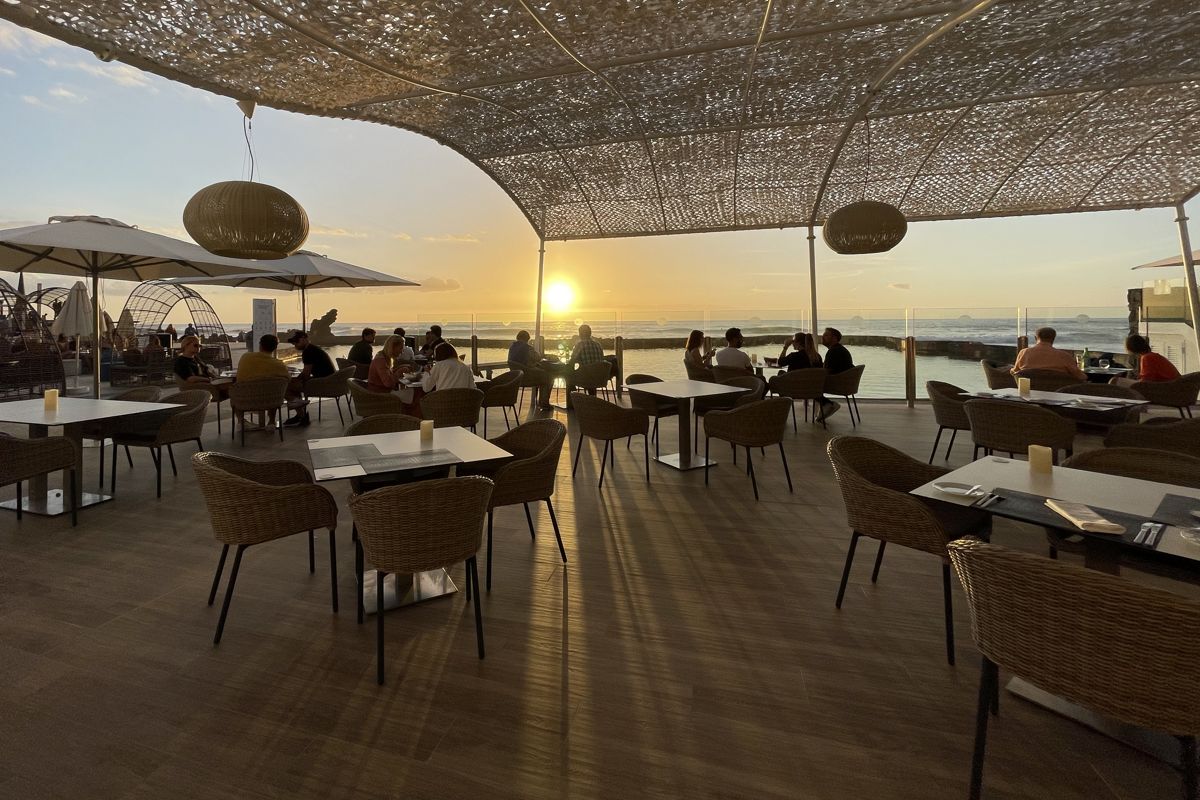 Persone che cenano al tramonto su una terrazza che si affaccia sul mare a Tenerife.