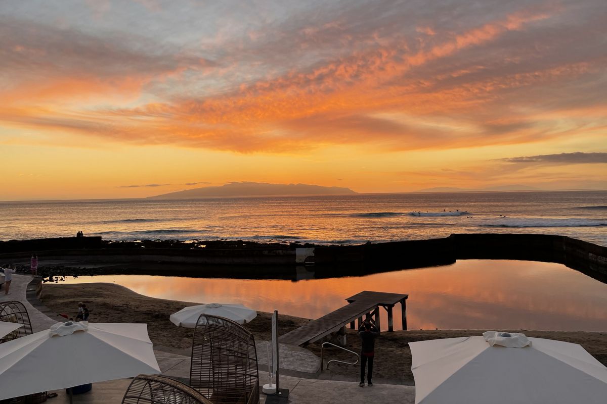 Il tramonto sull'oceano a Tenerife con cieli arancioni e ombrelli in primo piano.