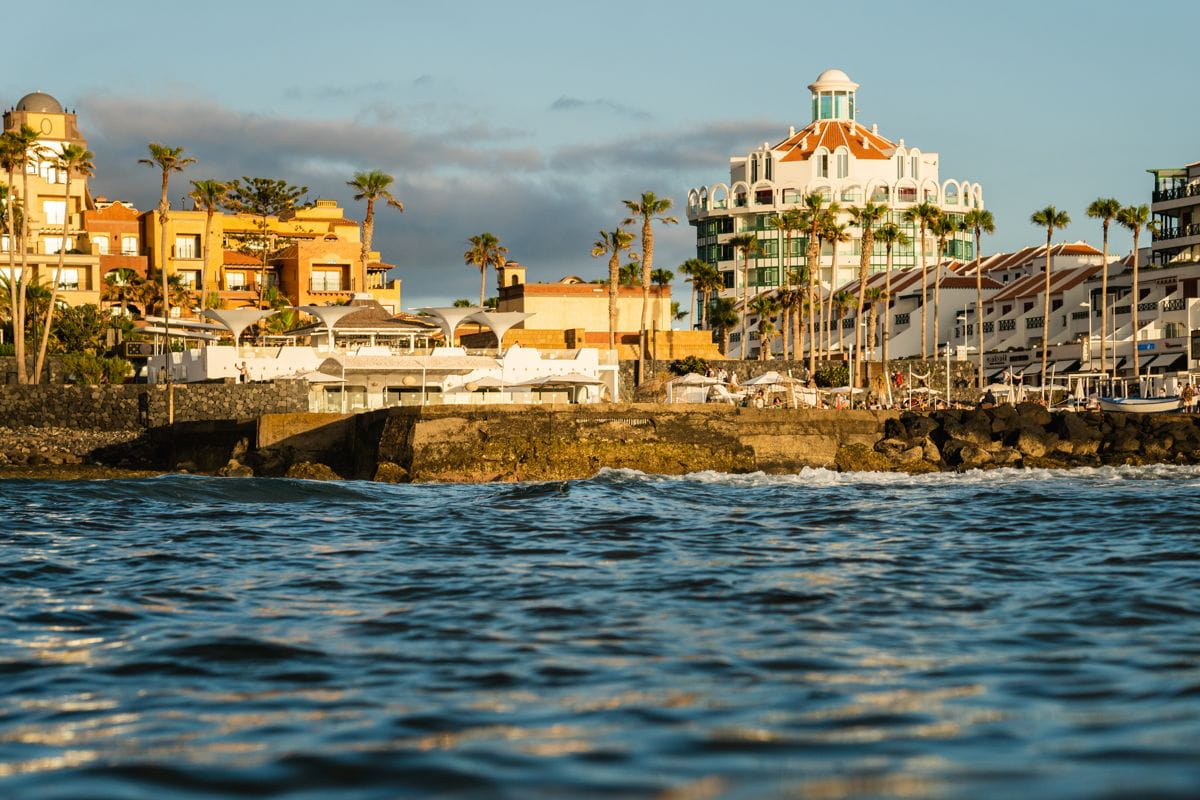 Vista della costa di Tenerife al tramonto con edifici e palme.