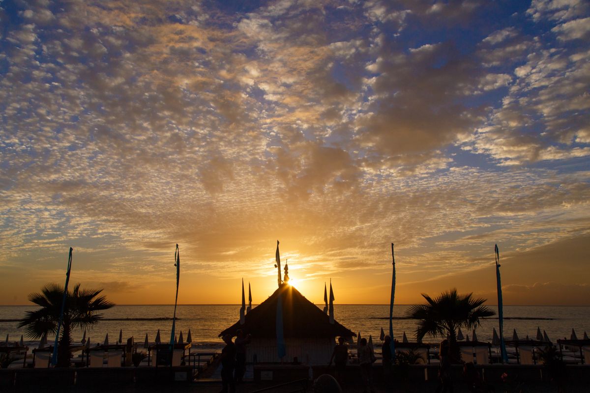 Il tramonto sulla spiaggia con ombrelloni e palme a Tenerife.