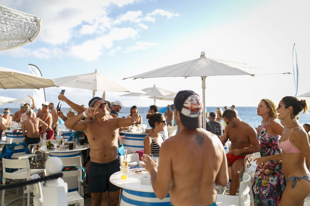 Persone che si godono una festa in spiaggia a Tenerife, con ombrelloni e tavoli.