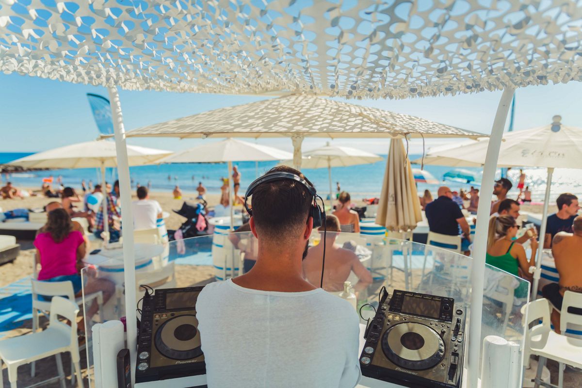 DJ che suona musica su una spiaggia a Tenerife con persone che si godono il mare.