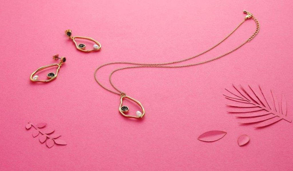 Collana e orecchini d'oro con perle su sfondo rosa e decorazioni a forma di foglie.