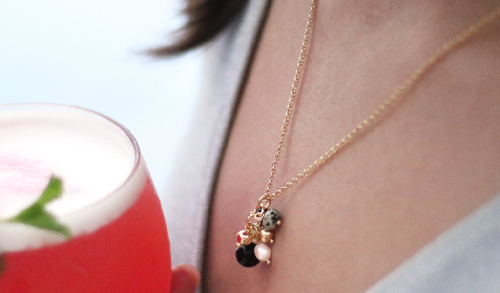 Collana con ciondoli e bevanda rosa in un bicchiere con una persona.