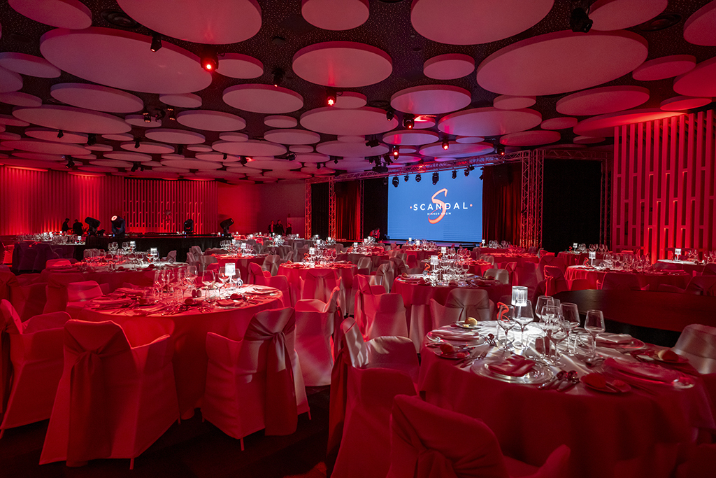 Sala eventi con tavoli decorati e schermo con il logo SCANDAL Show Tenerife.
