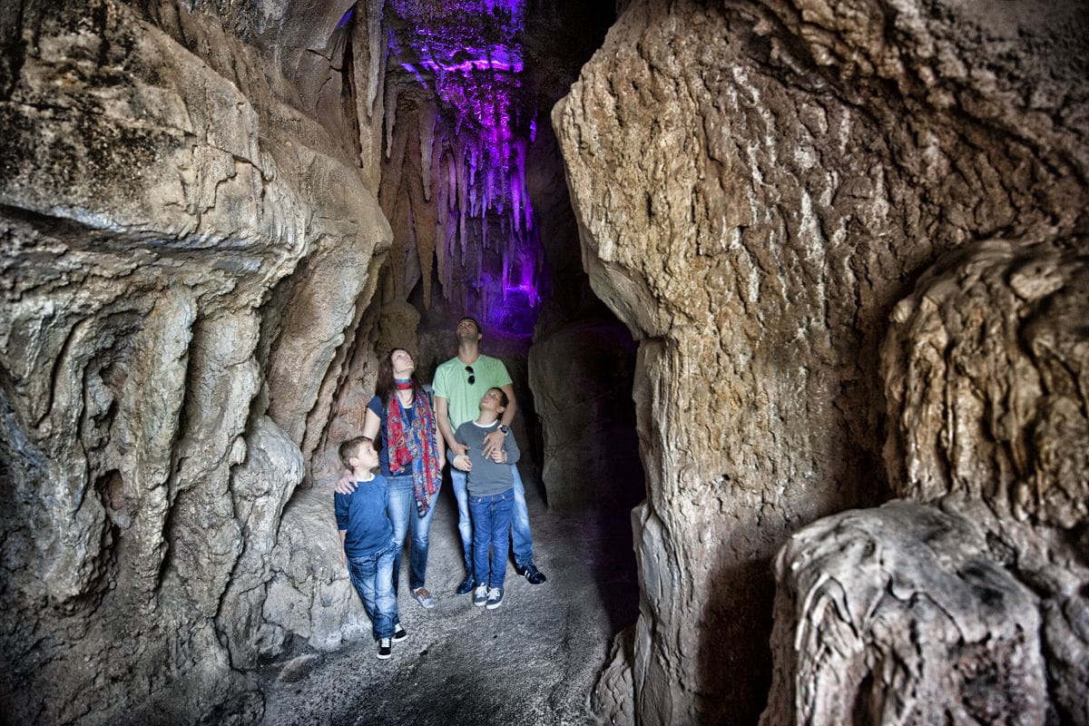 Famiglia che esplora una grotta a Tenerife, con luci viola che mettono in risalto l'interno.