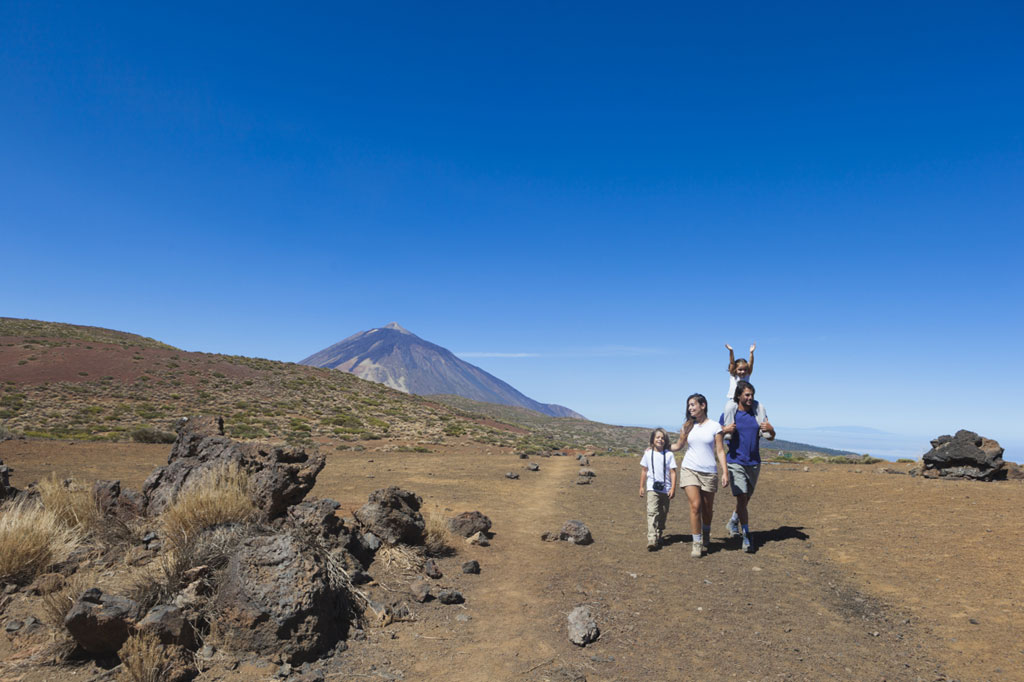 Famiglia che cammina lungo un sentiero sul Monte Teide, Tenerife, con il vulcano sullo sfondo.