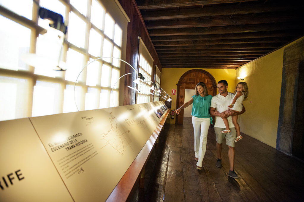 Famiglia che visita un museo a Tenerife, osserva una mostra illuminata in un corridoio di legno.