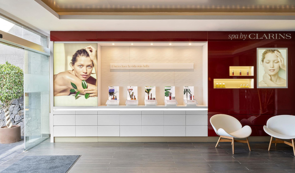 Accoglienza della spa Clarins a Tenerife con poster di modelli e prodotti. Testo: I clarini rendono la vita più bella.