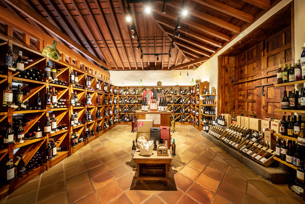 Cantina a Tenerife con scaffali pieni di bottiglie di vino e soffitto in legno.
