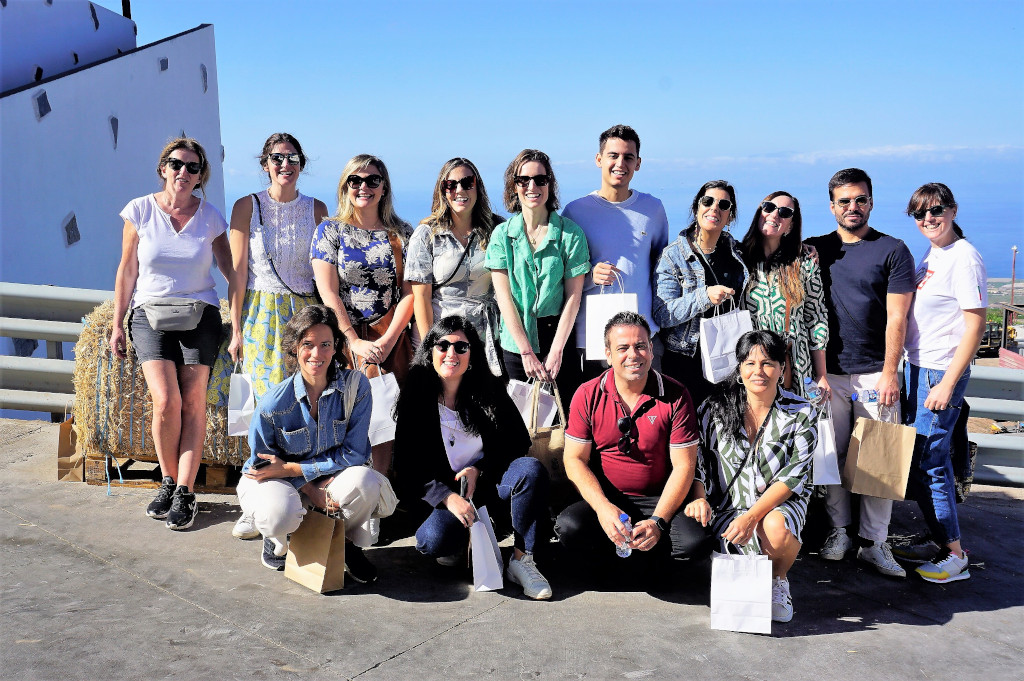 Gruppo di persone sorridenti davanti al mare in un luogo a Tenerife, con sacchetti regalo.