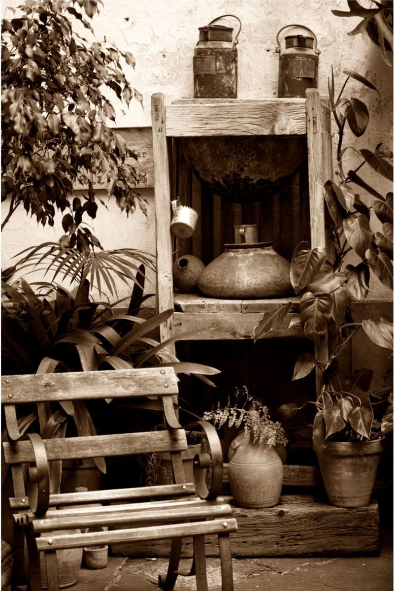Panchina di legno circondata da piante e oggetti metallici in un cortile rustico a Tenerife.