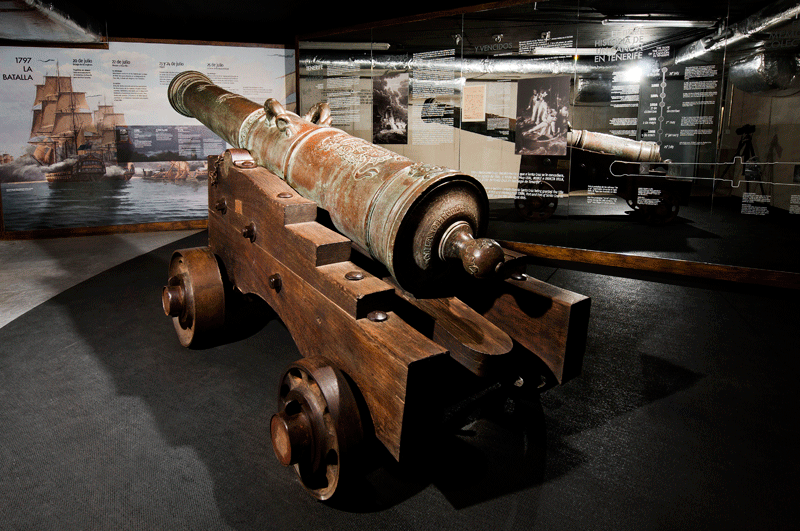 Antico cannone esposto in un museo a Tenerife, con pannelli informativi dietro.