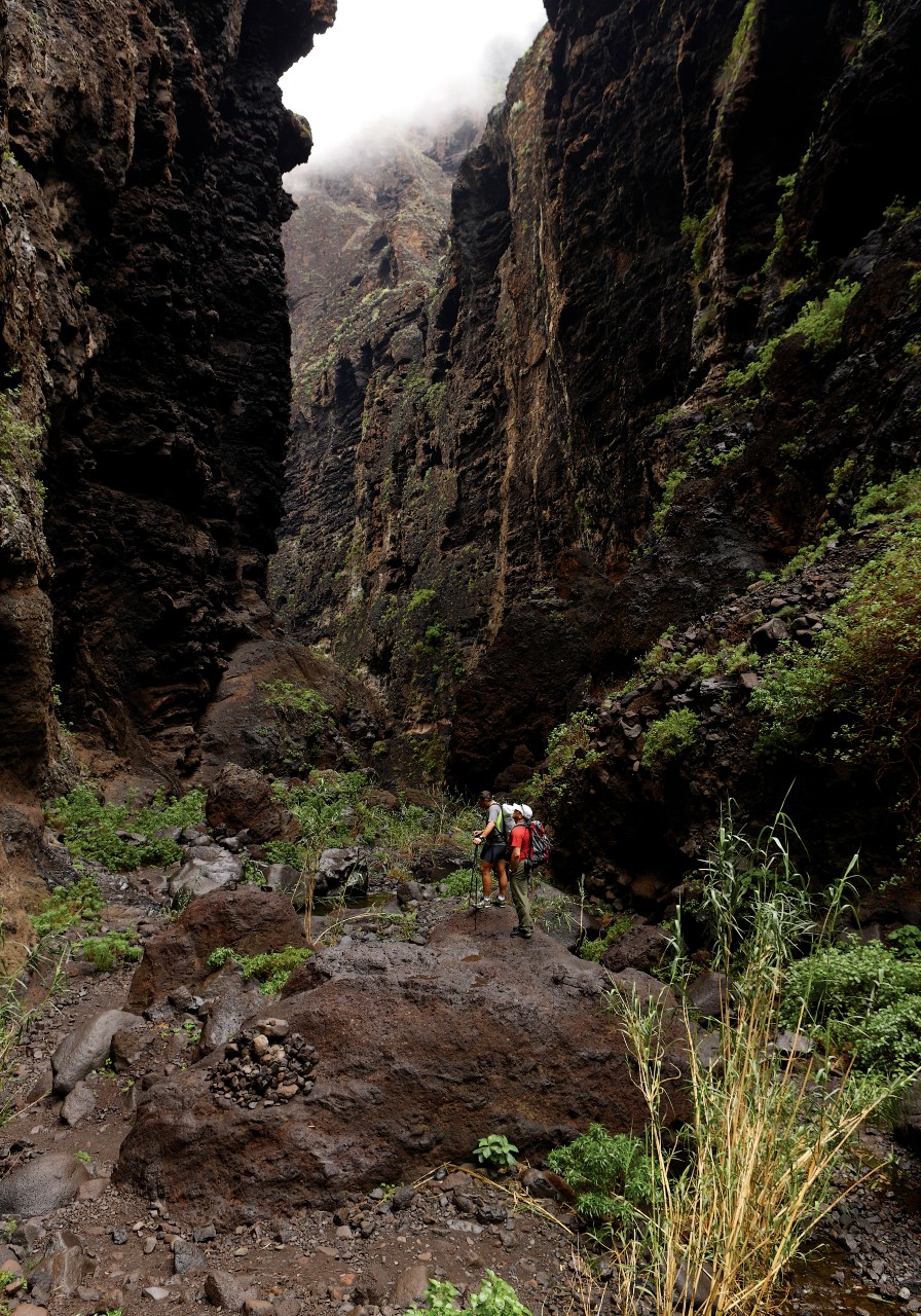 Due persone che camminano attraverso il Barranco de Masca a Tenerife circondate da alte pareti rocciose.