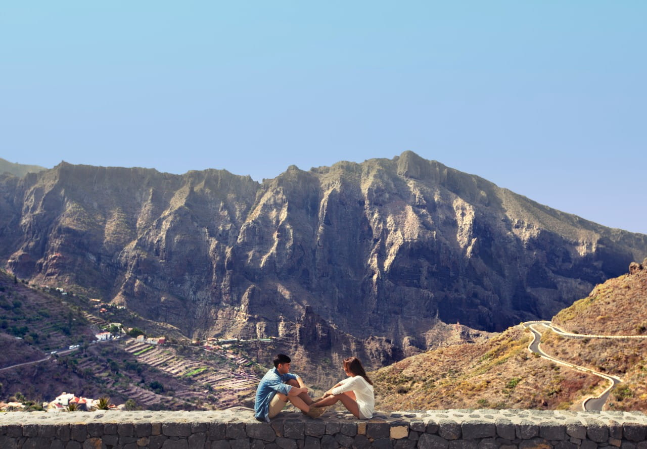 Persone sedute davanti ai monti Masca a Tenerife, con un sentiero tortuoso sullo sfondo.