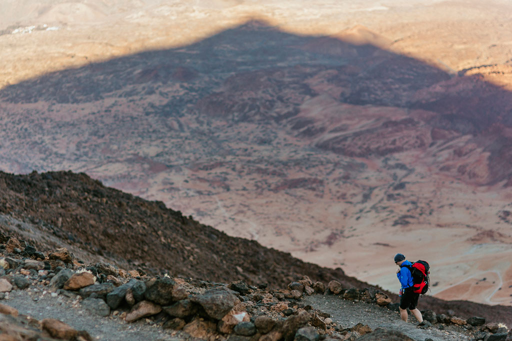 Persona che cammina su un sentiero roccioso sul Monte Teide, Tenerife, con paesaggio arido sullo sfondo.