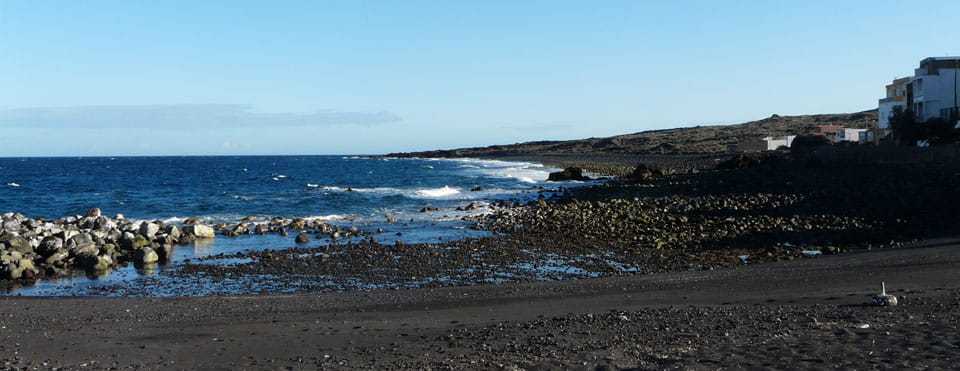 Costa rocciosa e mare a Playa Ajabo, Tenerife, con edifici sullo sfondo.
