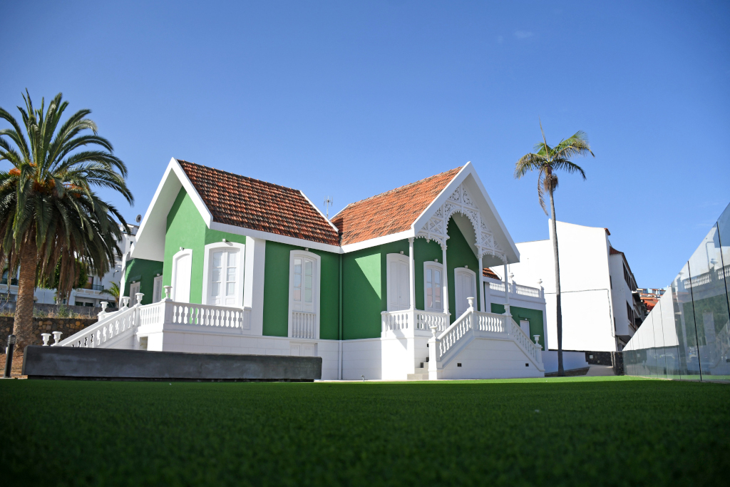 Vecchia casa verde e bianca con tetto rosso a Tenerife, circondata da palme e prati.