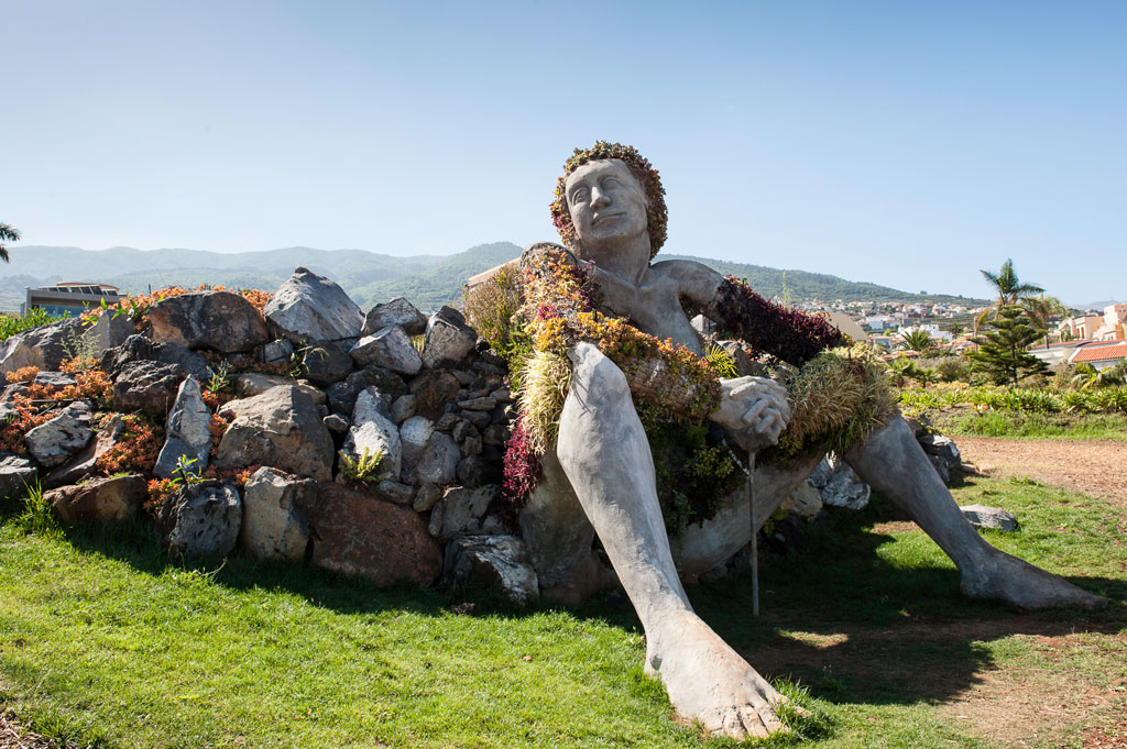 Scultura di una donna seduta coperta di piante in un parco a Tenerife.