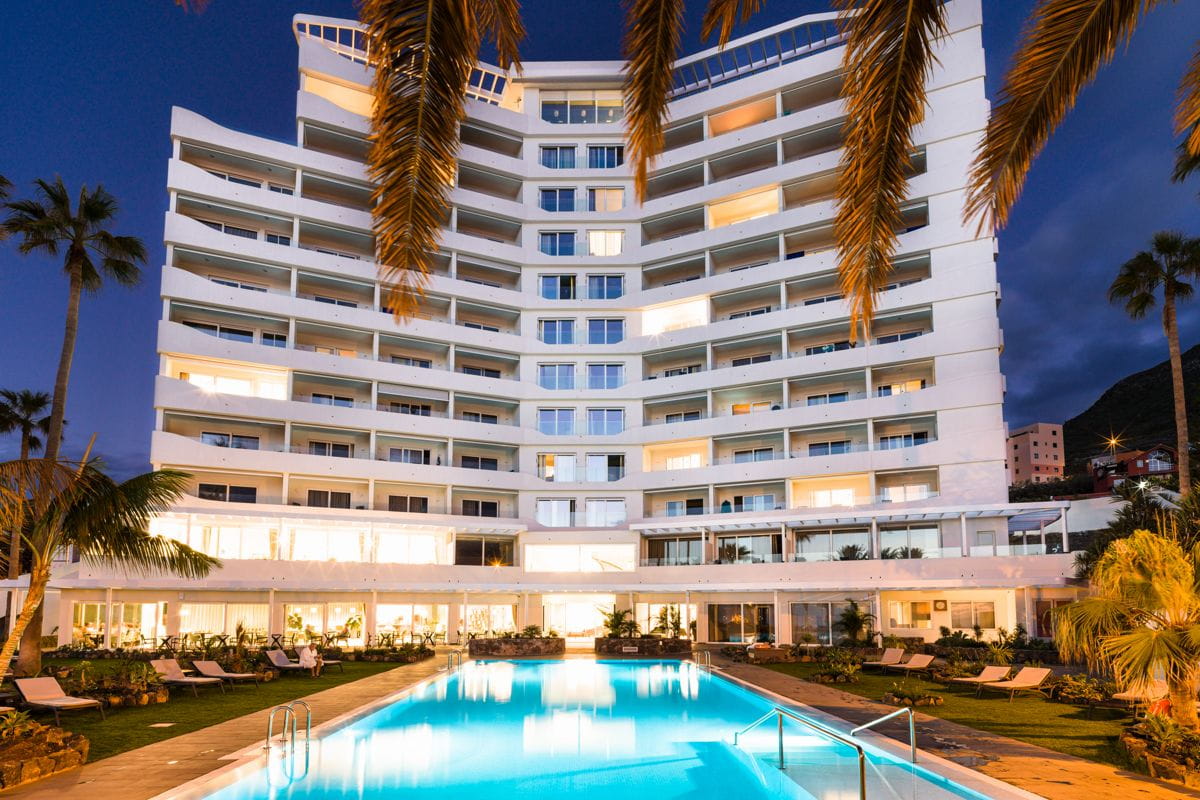 Edificio con piscina illuminata al crepuscolo a Tenerife, circondato da palme.